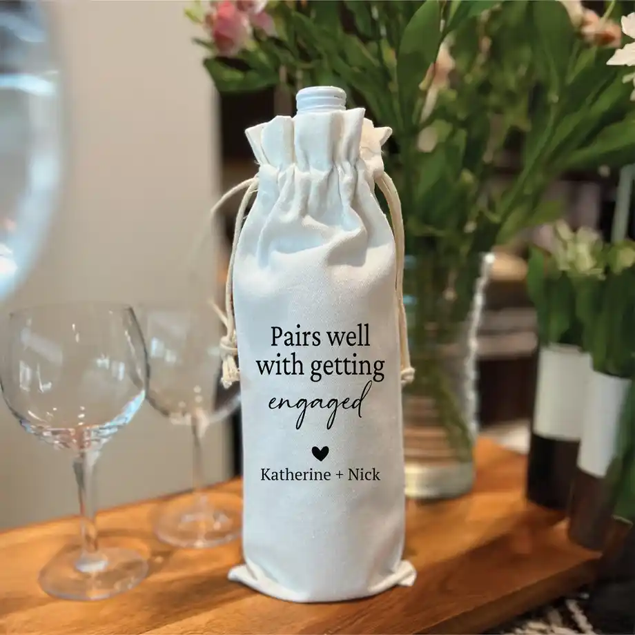 A stylish wine bag with the phrase "Pairs Well with Getting Engaged" printed on it, making it a perfect addition to engagement gift ideas. A fun and thoughtful way to celebrate a newly engaged couple with their favorite bottle of wine.