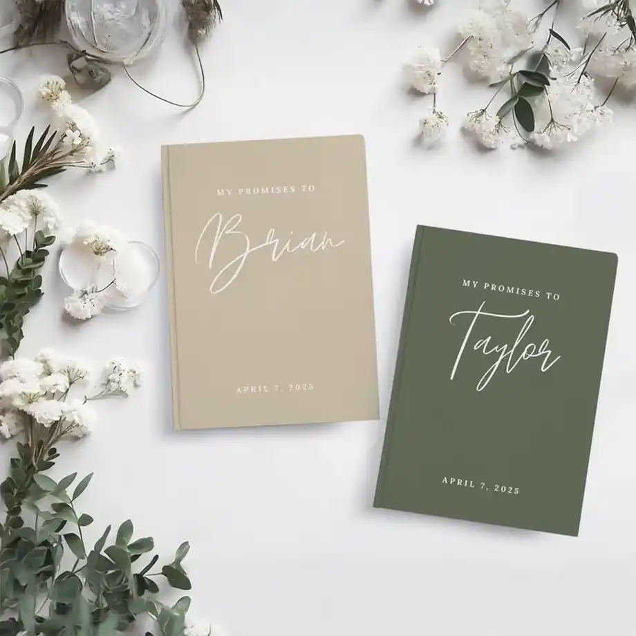 A set of two personalized promise journals in neutral and green tones, featuring elegant script with names and a wedding date. Surrounded by white flowers and candles, these keepsake books make sentimental engagement gift ideas for couples.