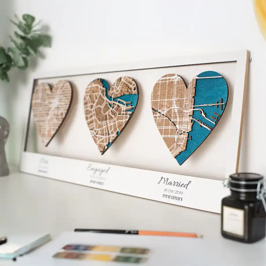 A beautifully crafted wooden frame featuring three heart-shaped maps representing the locations of a couple’s first meeting, engagement, and wedding. This sentimental and unique artwork is a perfect choice for engagement gift ideas, capturing the couple’s love story in a meaningful and decorative keepsake.