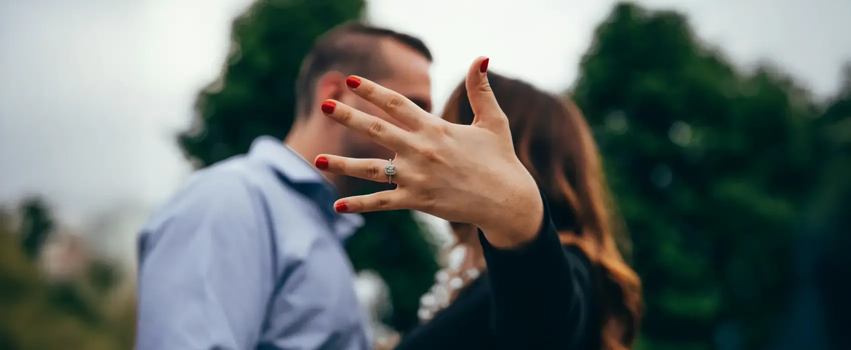 A newly engaged woman proudly shows off her engagement ring while embracing her fiancé. Discover thoughtful engagement gift ideas to celebrate this special moment.