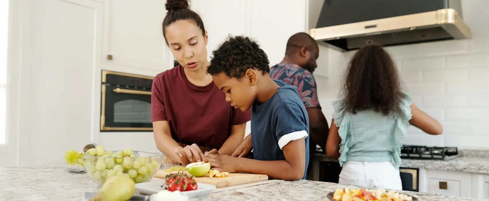 Mom and kids preparing healthy snacks for kids together in the kitchen with fresh fruits and vegetables on the counter.