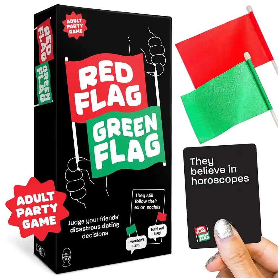 A black box featuring the Red Flag Green Flag party game with bold red and green flags on the packaging The game challenges players to judge dating decisions and identify red flags in relationships A hand holds a black card that says They believe in horoscopes with two small red and green flags placed beside the box highlighting red flags in relationship dynamics