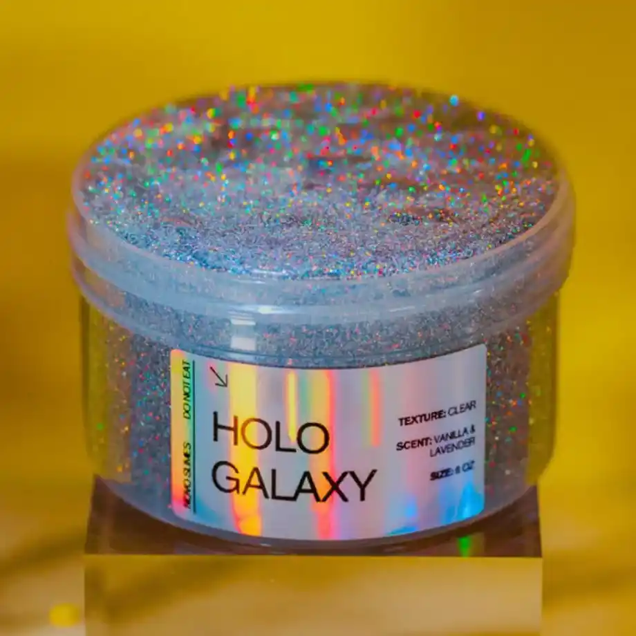 A jar of sparkling silver holographic slime labeled “HOLO GALAXY,” featuring a clear texture with vanilla and lavender scent. A fun reminder of why parents often search how to get slime out of clothes after glittery messes like this one!